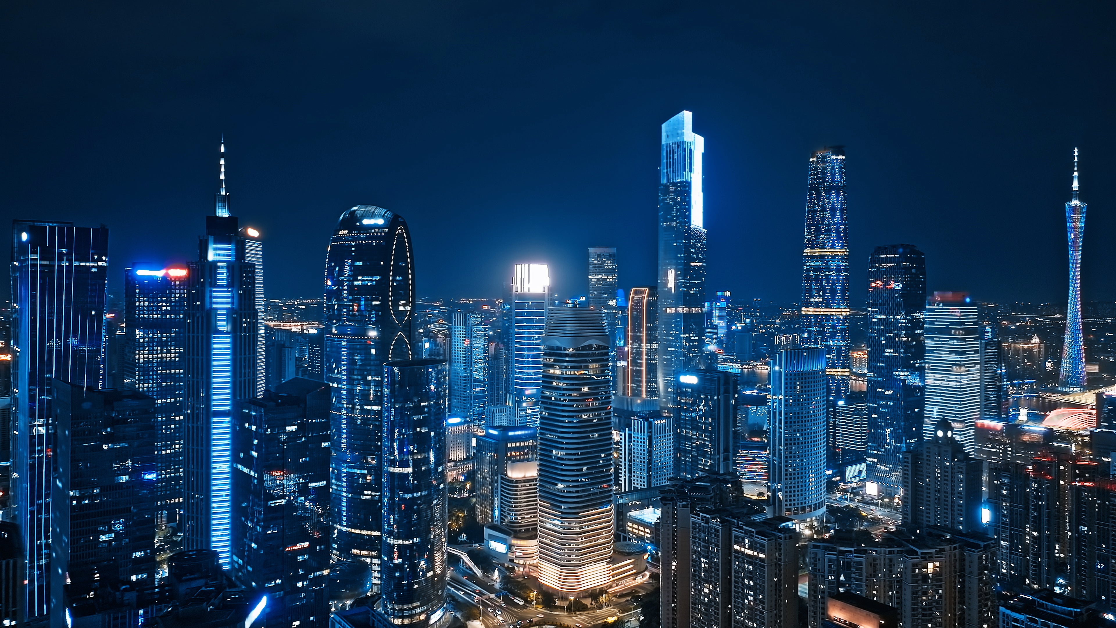 Aerial drone fly‑by image of the Guangzhou skyline at night, featuring Canton Tower and the two Guangzhou Twin Towers - the Guangzhou CTF Finance Centre and the Guangzhou International Finance Center (IFC) - illuminated in blue.