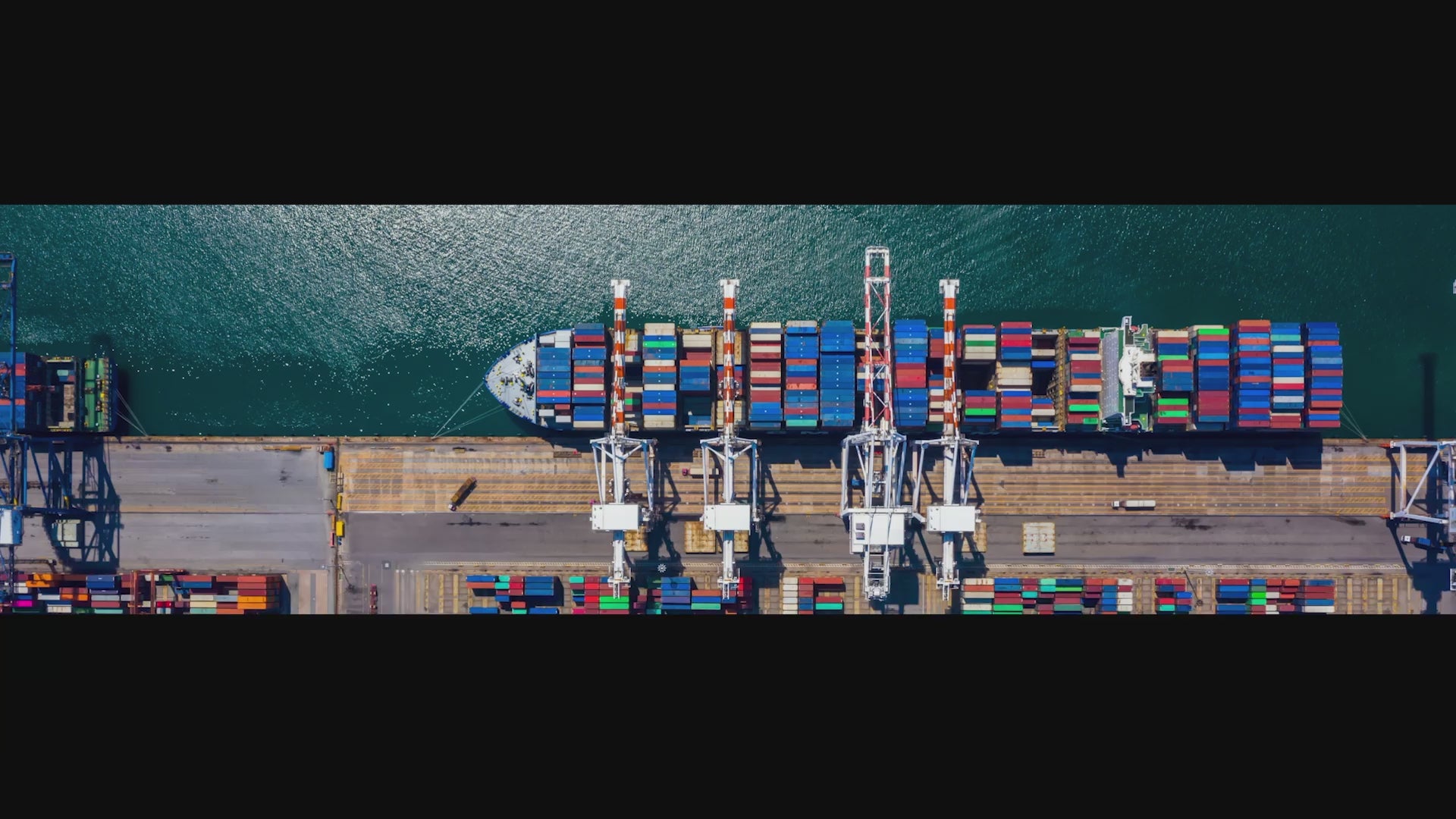 Aerial top view video of a container ship in port, with cranes loading and off-loading containers.